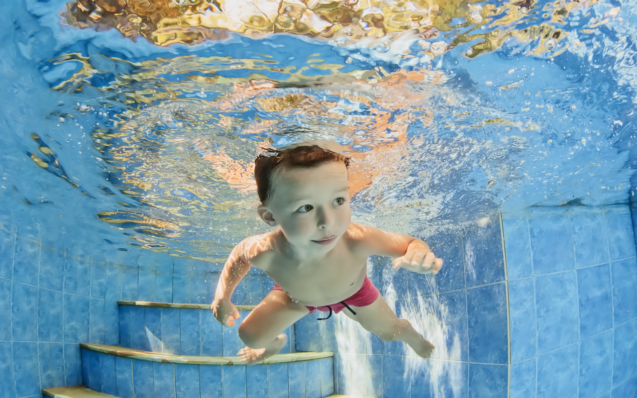 Маленький мальчик плавает под водой в бассейне