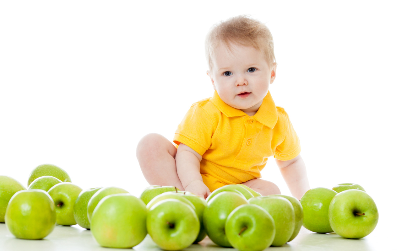 Маленький мальчик с зелеными яблоками на белом фоне