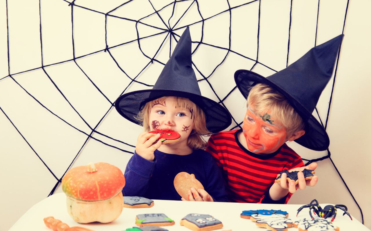 Маленькие дети в костюмах на Хэллоуин едят праздничные сладости