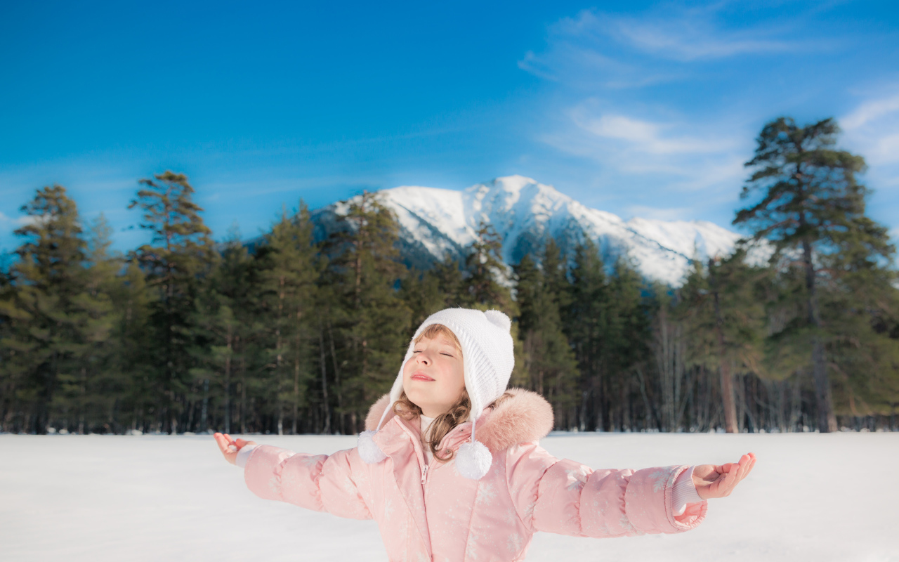 Маленькая девочка в розовой куртке на фоне гор зимой