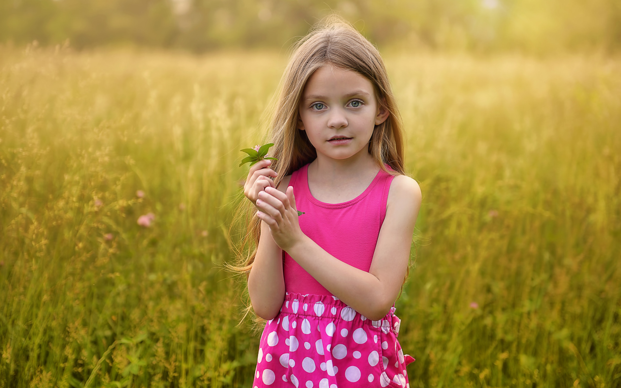 Маленькая длинноволосая девочка в розовом сарафане на поле