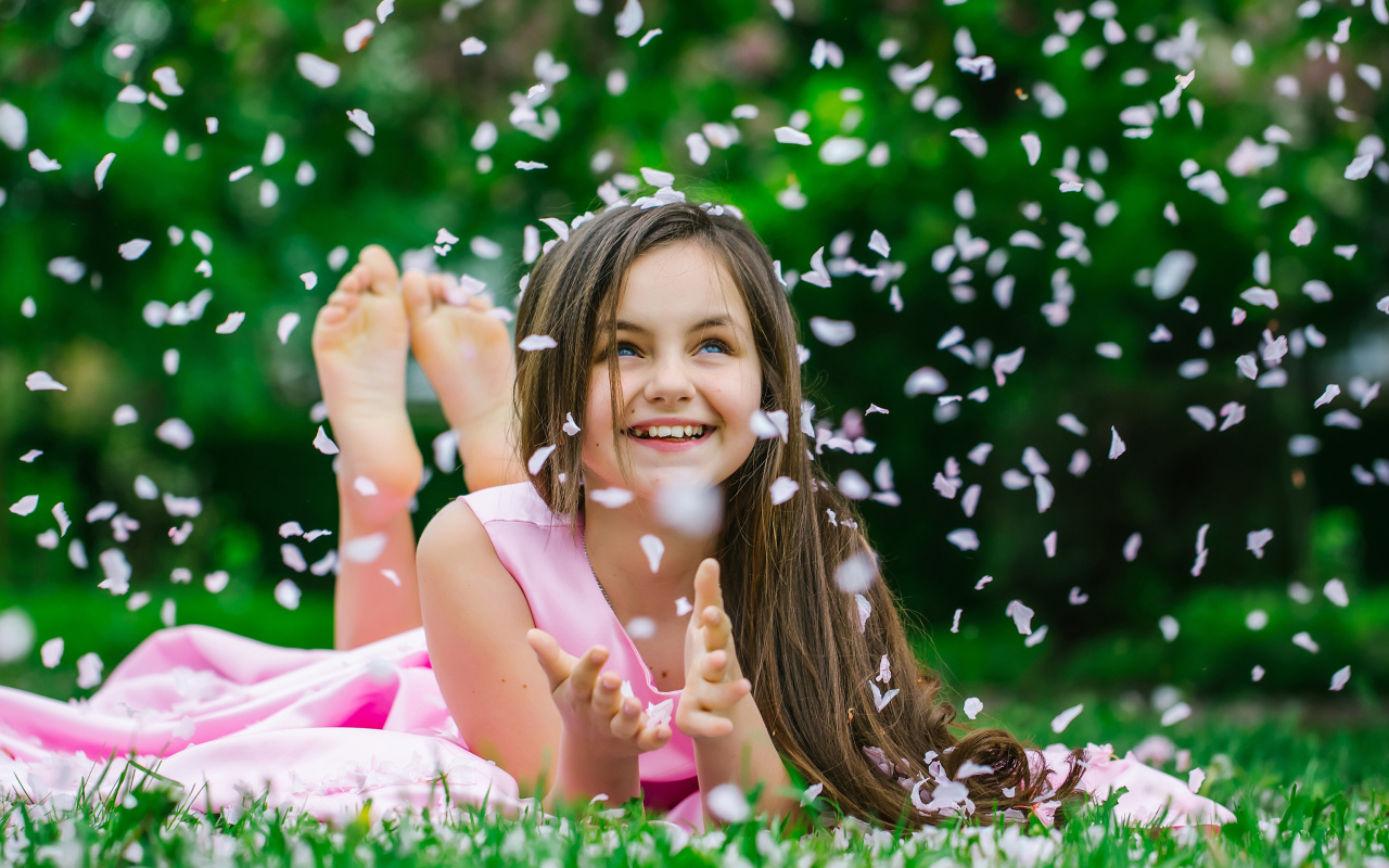 Маленькая улыбающаяся девочка шатенка ловит лепестки