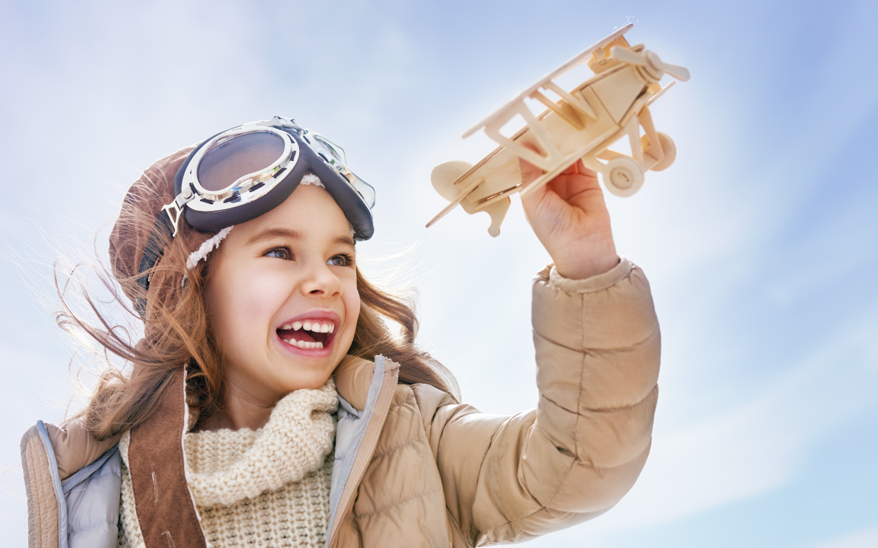 Маленькая улыбающаяся девочка с самолетом в руках 