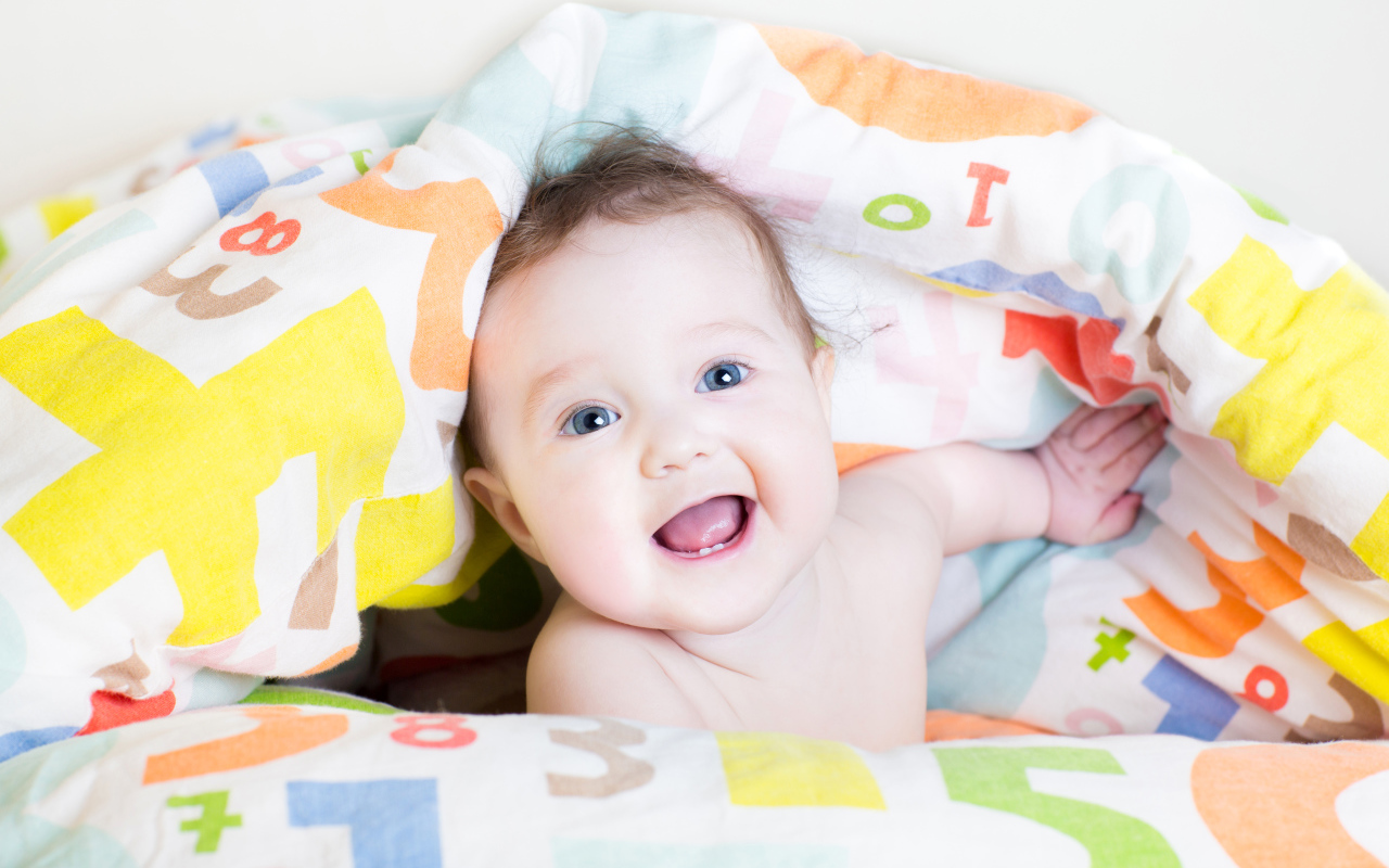 Улыбающийся голубоглазый ребенок под разноцветным покрывалом