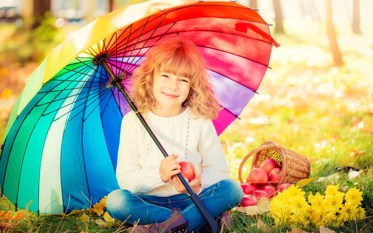 Улыбающаяся девочка под сидит под разноцветным зонтом