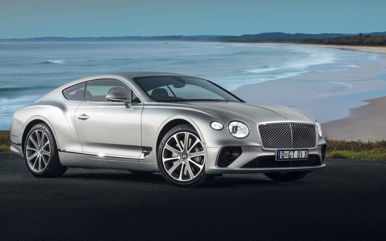 Серебристый автомобиль Bentley Continental GT 2018 года на фоне океана 