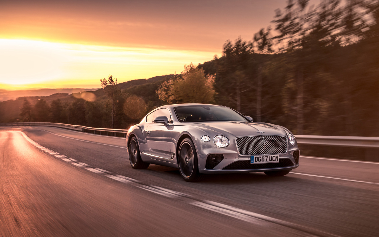Серебристый автомобиль Bentley Continental GT 2018 года на фоне заката