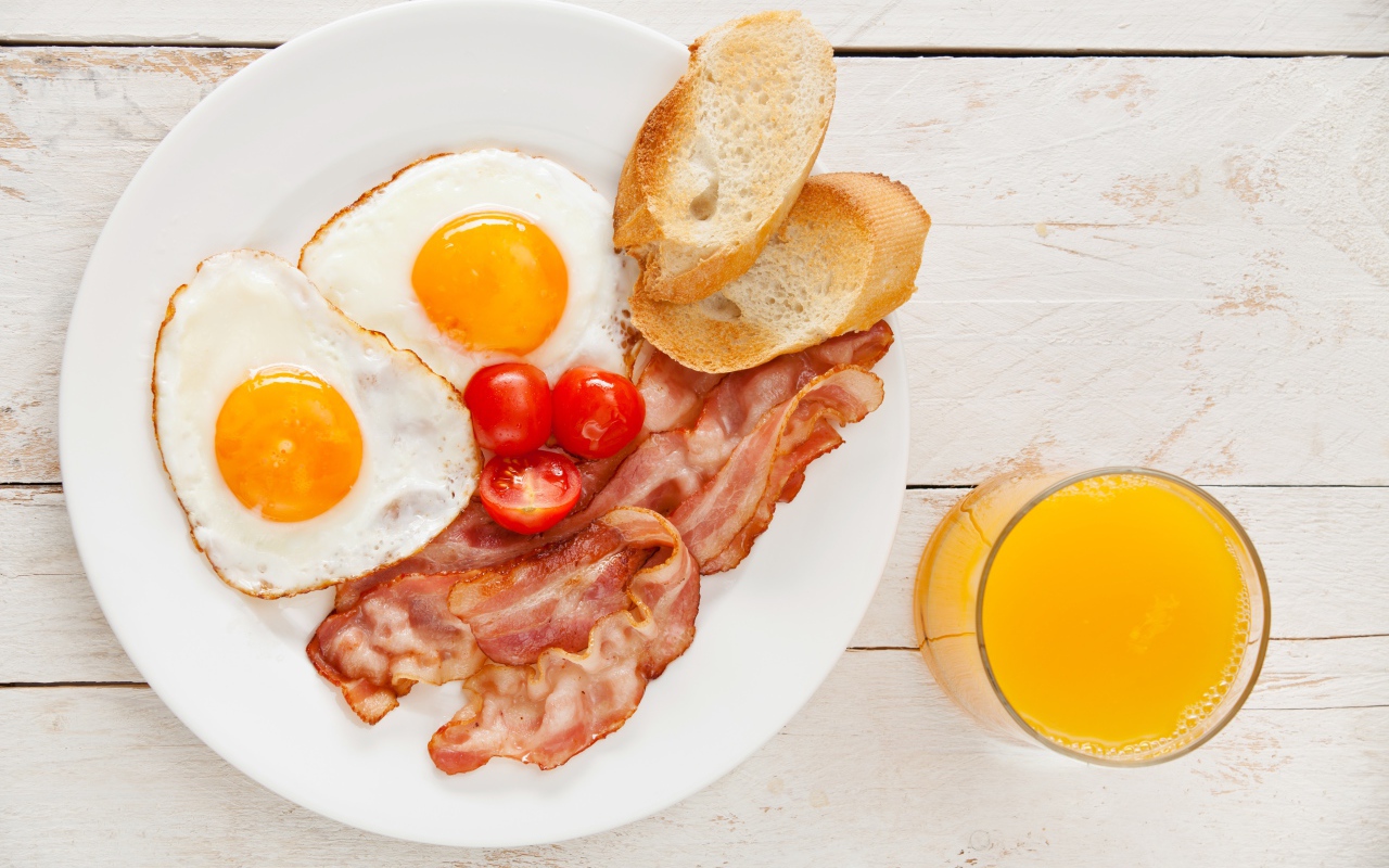 Яичница с беконом, гренками и помидорами на столе с соком 