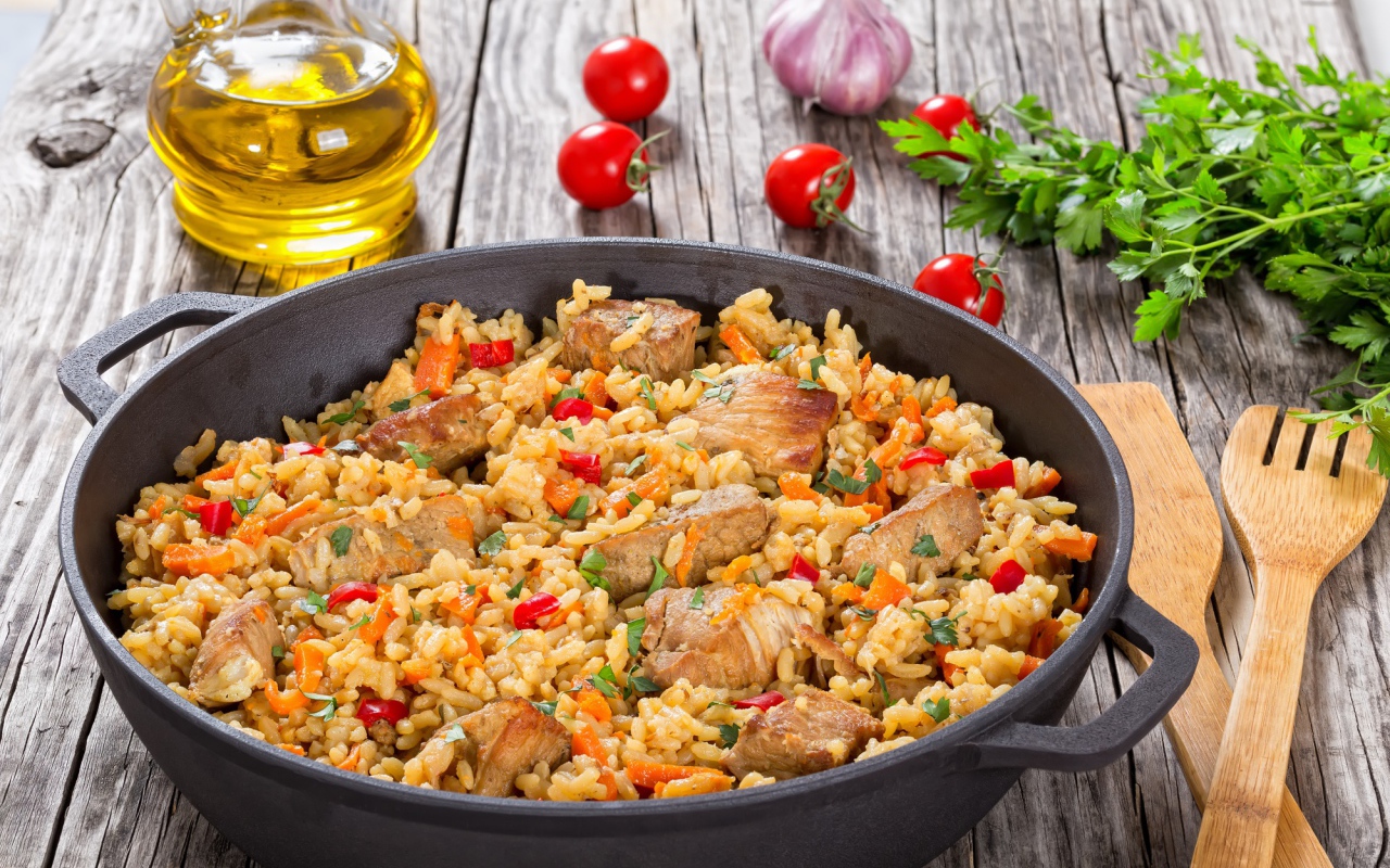 Плов с мясом на столе с помидорами и зеленью петрушки