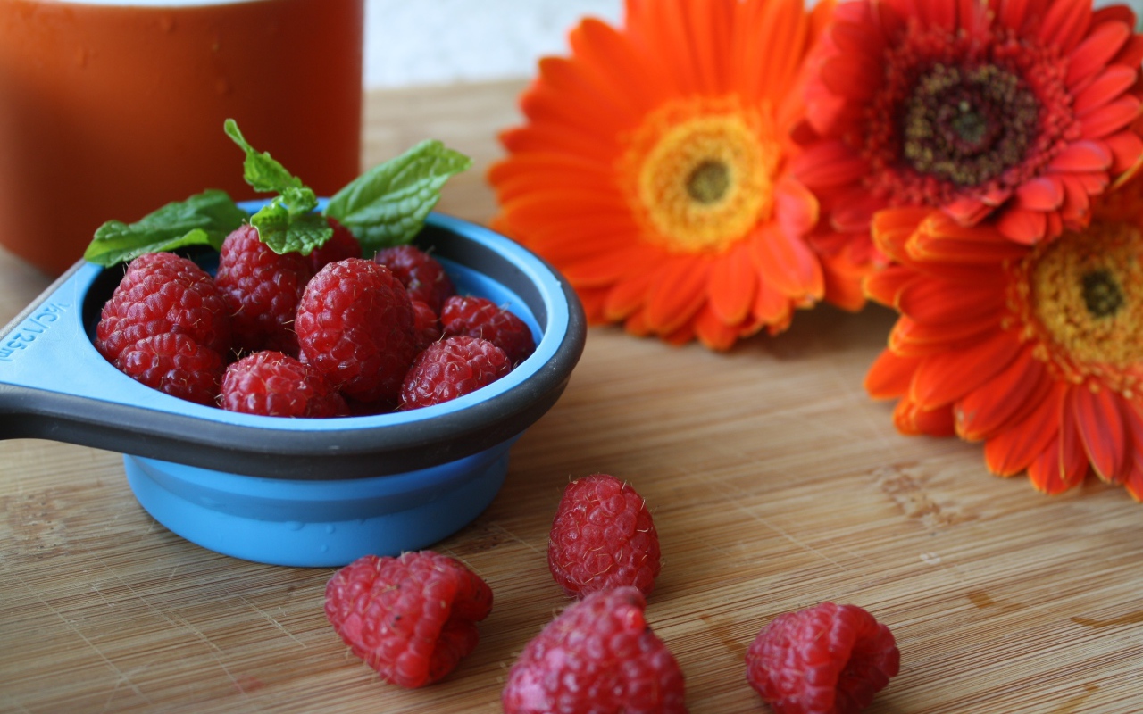 Свежая малина на столе с цветами герберы