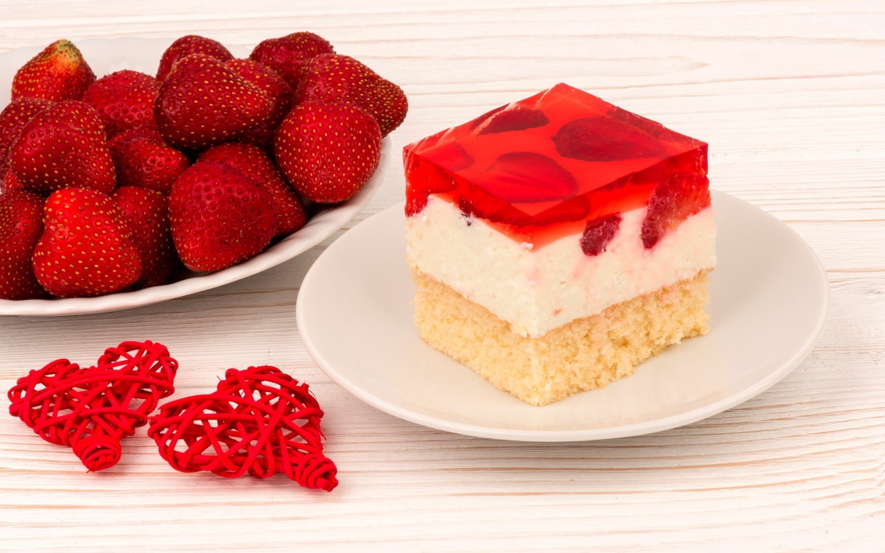 Пирожное на столе с клубникой и красными плетеными сердечками