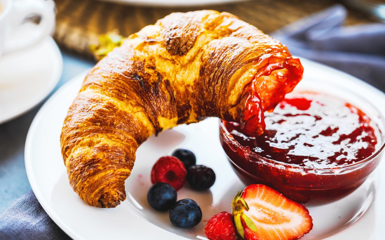 Круассан с джемом и ягодами на тарелке