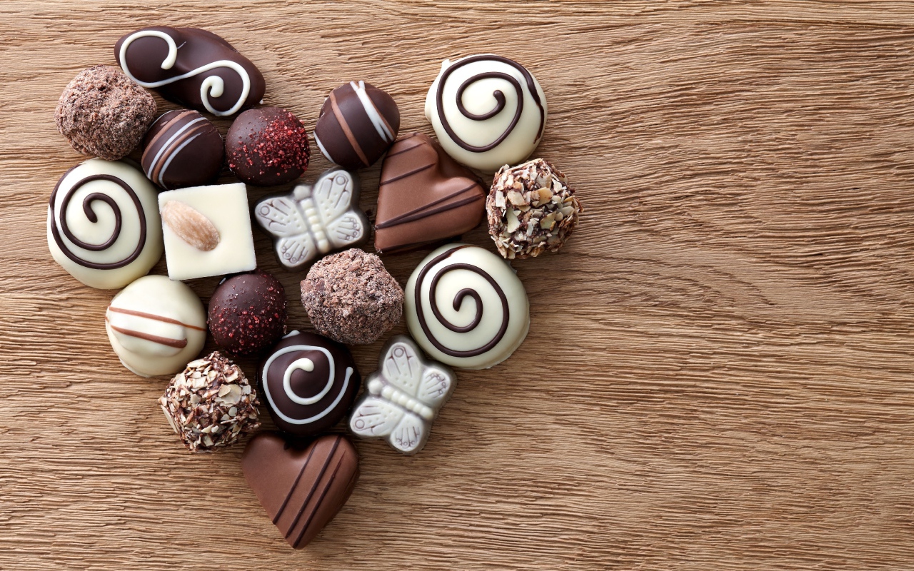 Сердце из шоколадных конфет ассорти на деревянном столе