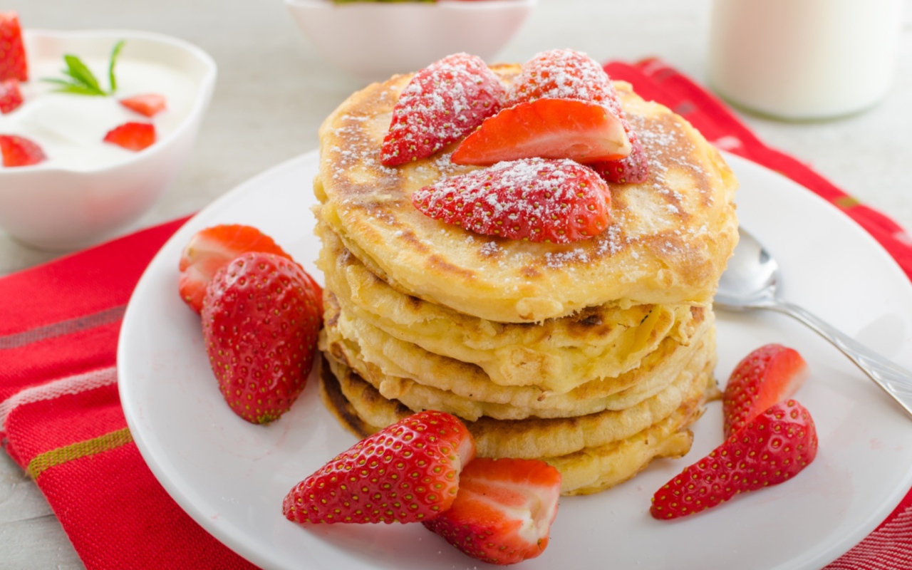 Оладьи с клубникой и сахарной пудрой на белой тарелке 