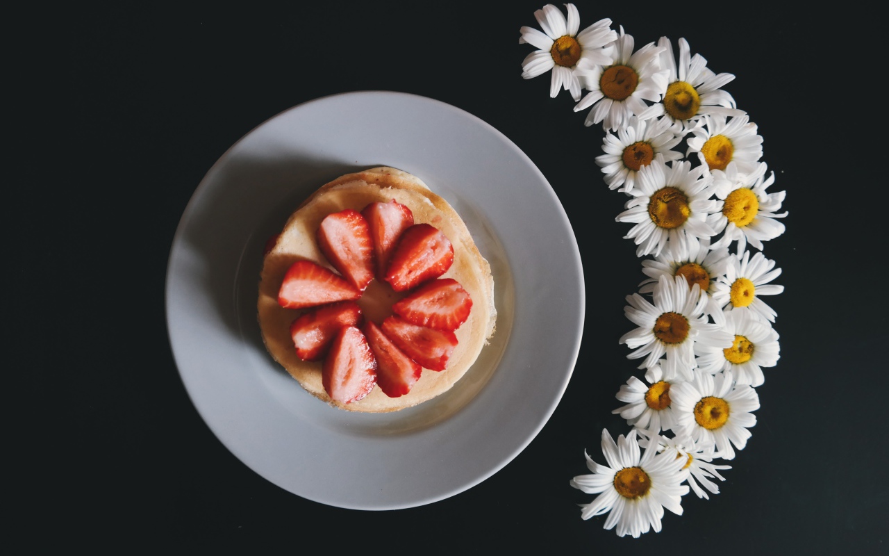 Оладьи с клубникой на тарелке на сером фоне с ромашками