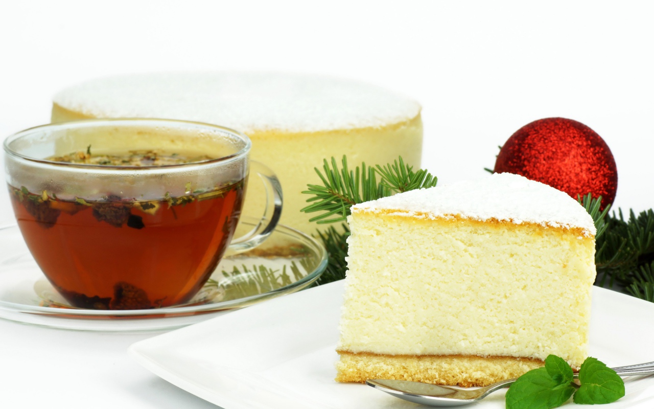 Кусок чизкейка на белой тарелке с чашкой чая на белом фоне