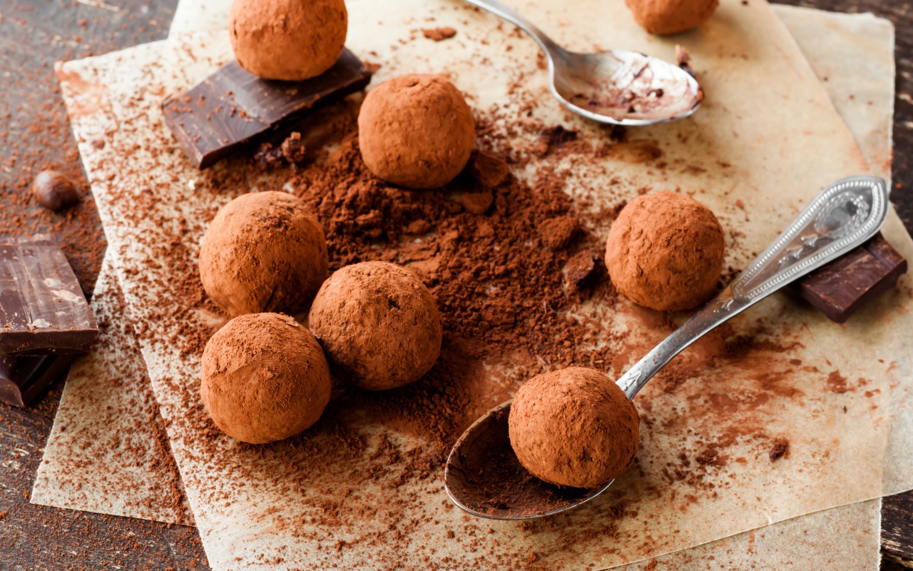 Круглые шоколадные конфеты в какао на столе с ложками