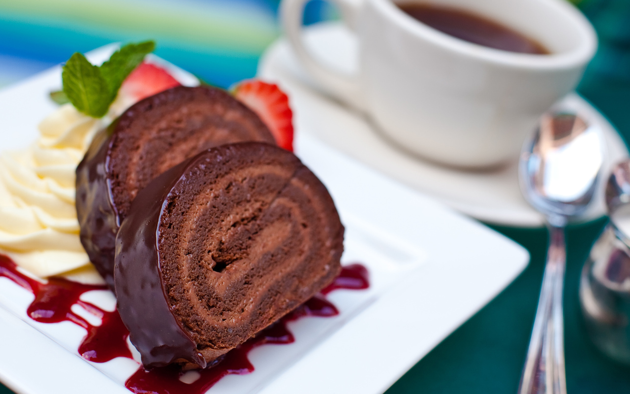 Сладкий рулет с клубничным джемом и чашкой чая на столе