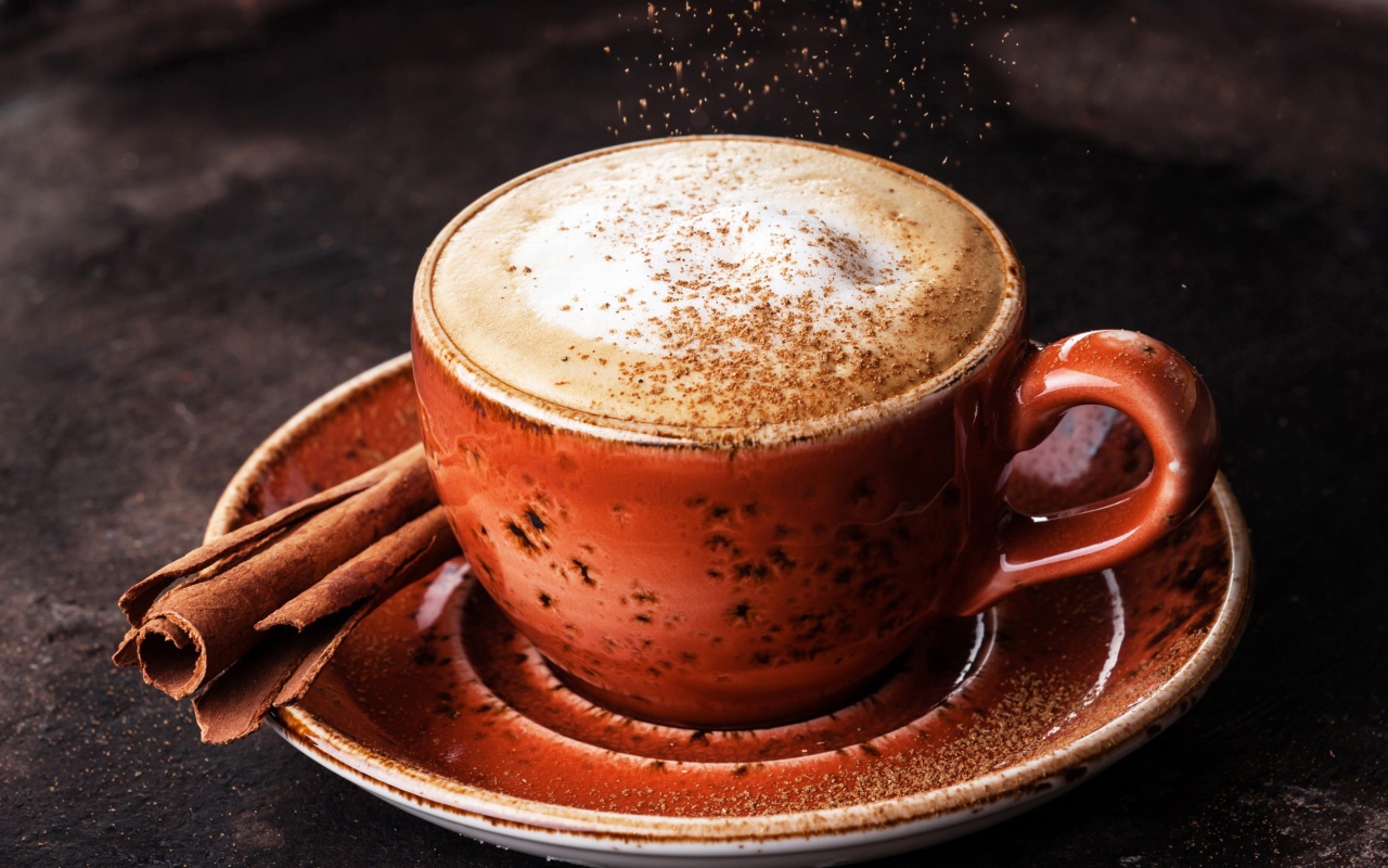 Чашка кофе с пенкой на блюдце с корицей
