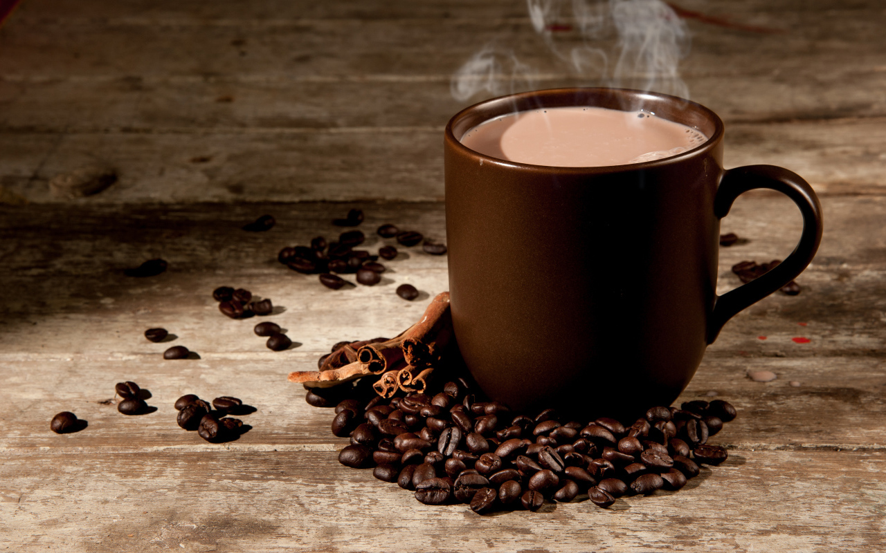 Чашка горячего кофе с молоком на столе с корицей и кофейными зернами