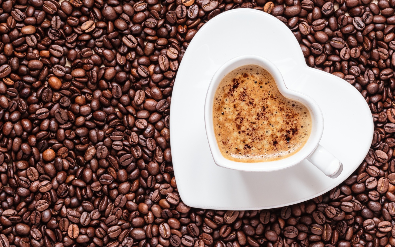 Белая чашка кофе в форме сердца стоит на кофейных зернах