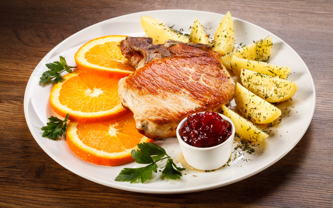 Кусок запеченного мяса с кусочками картофеля и апельсина и соусом