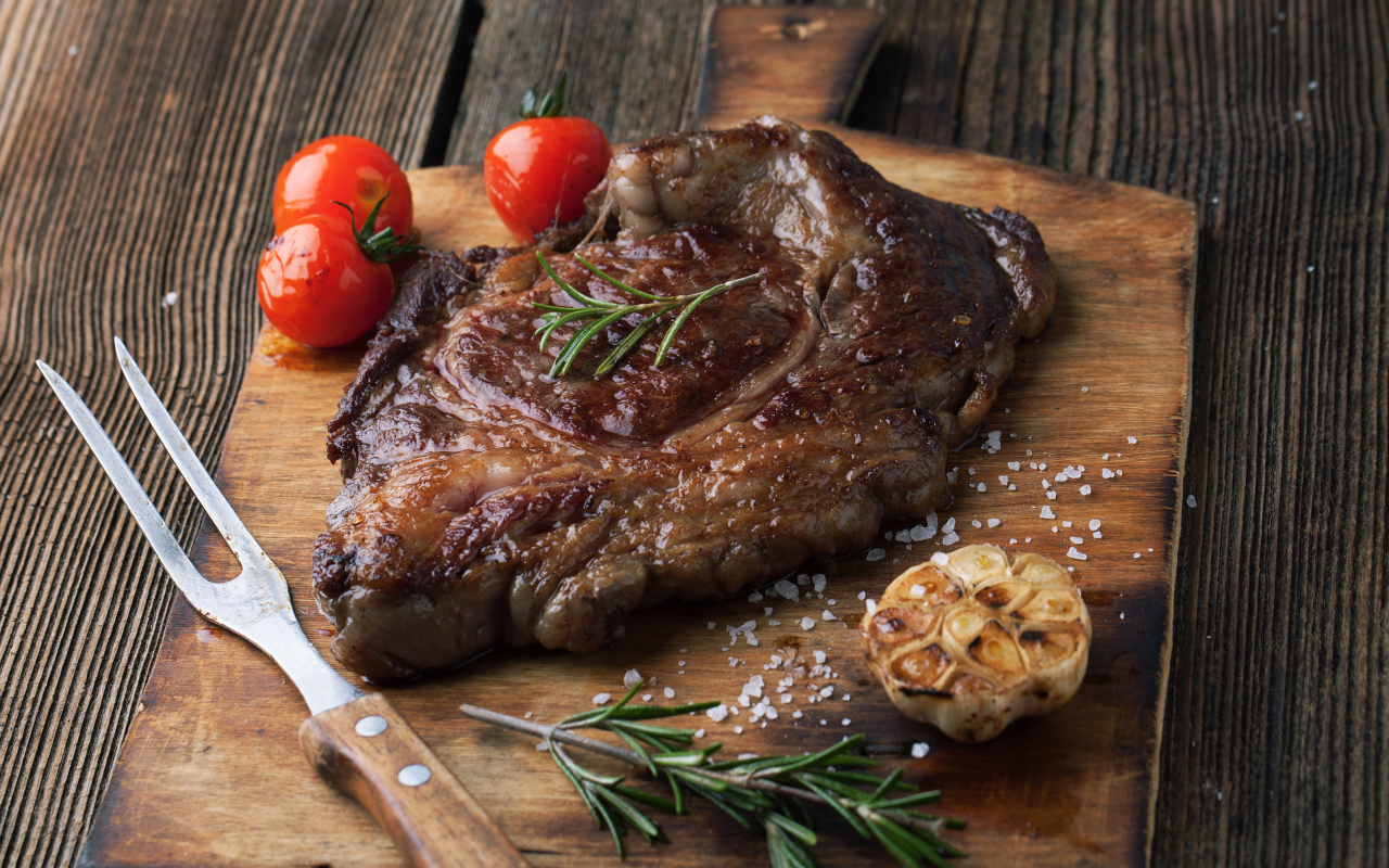 Кусок жареного мяса на разделочной доске с помидорами и чесноком