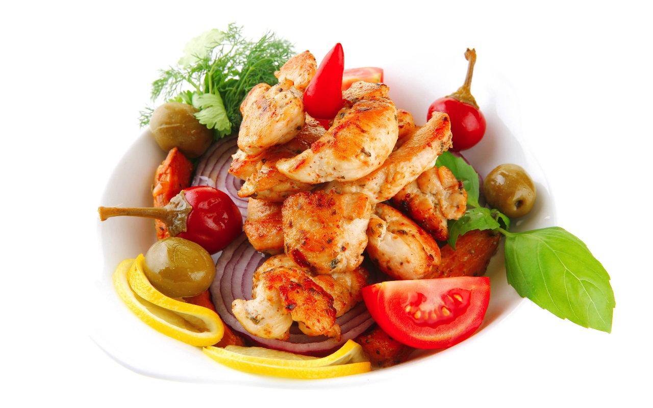 Жареные кусочки курицы на тарелке с овощами и зеленью 