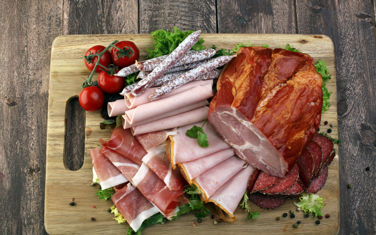 Мясная нарезка на разделочной доске с помидорами