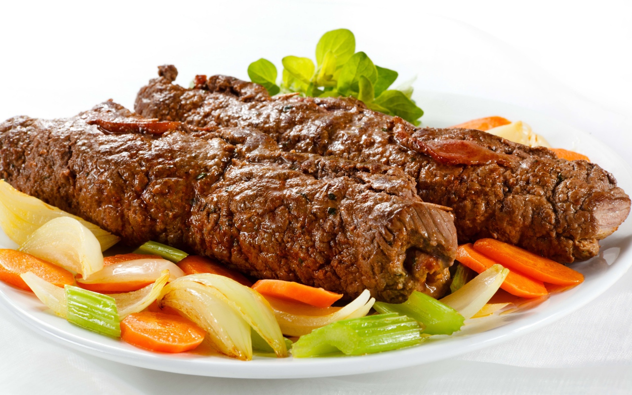 Свинина на тарелке с овощами на белом фоне