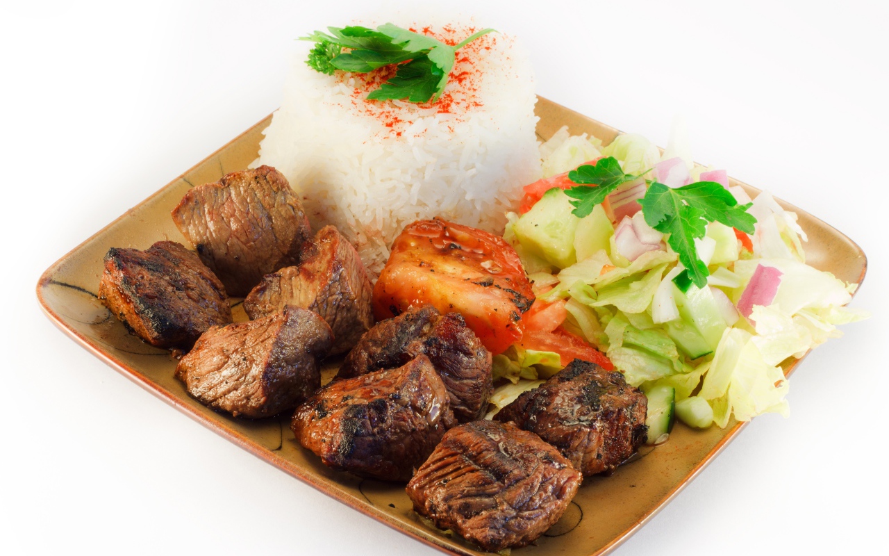 Шашлык с рисом и овощами в тарелке на белом фоне