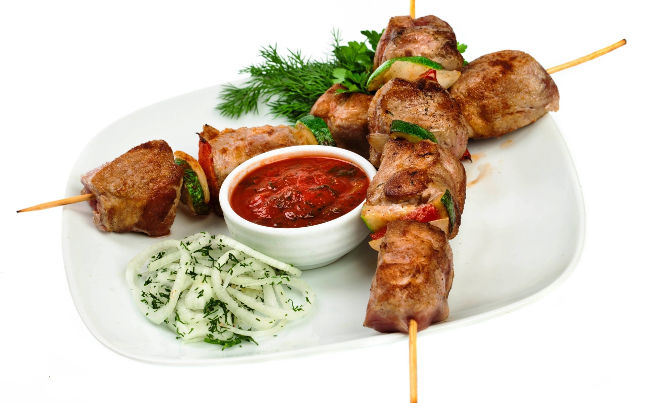 Шашлык на белой тарелке с соусом, зеленью и луком