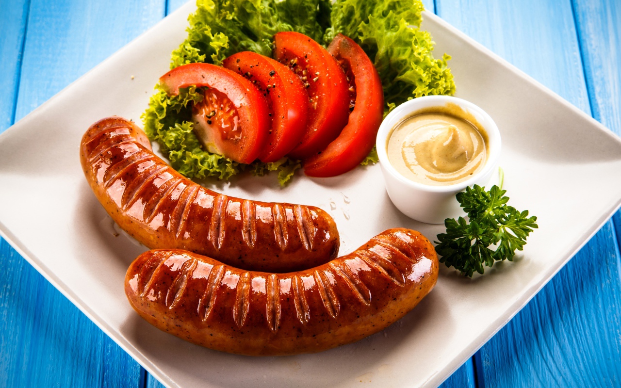 Две сосиски гриль на тарелке с овощами и горчицей