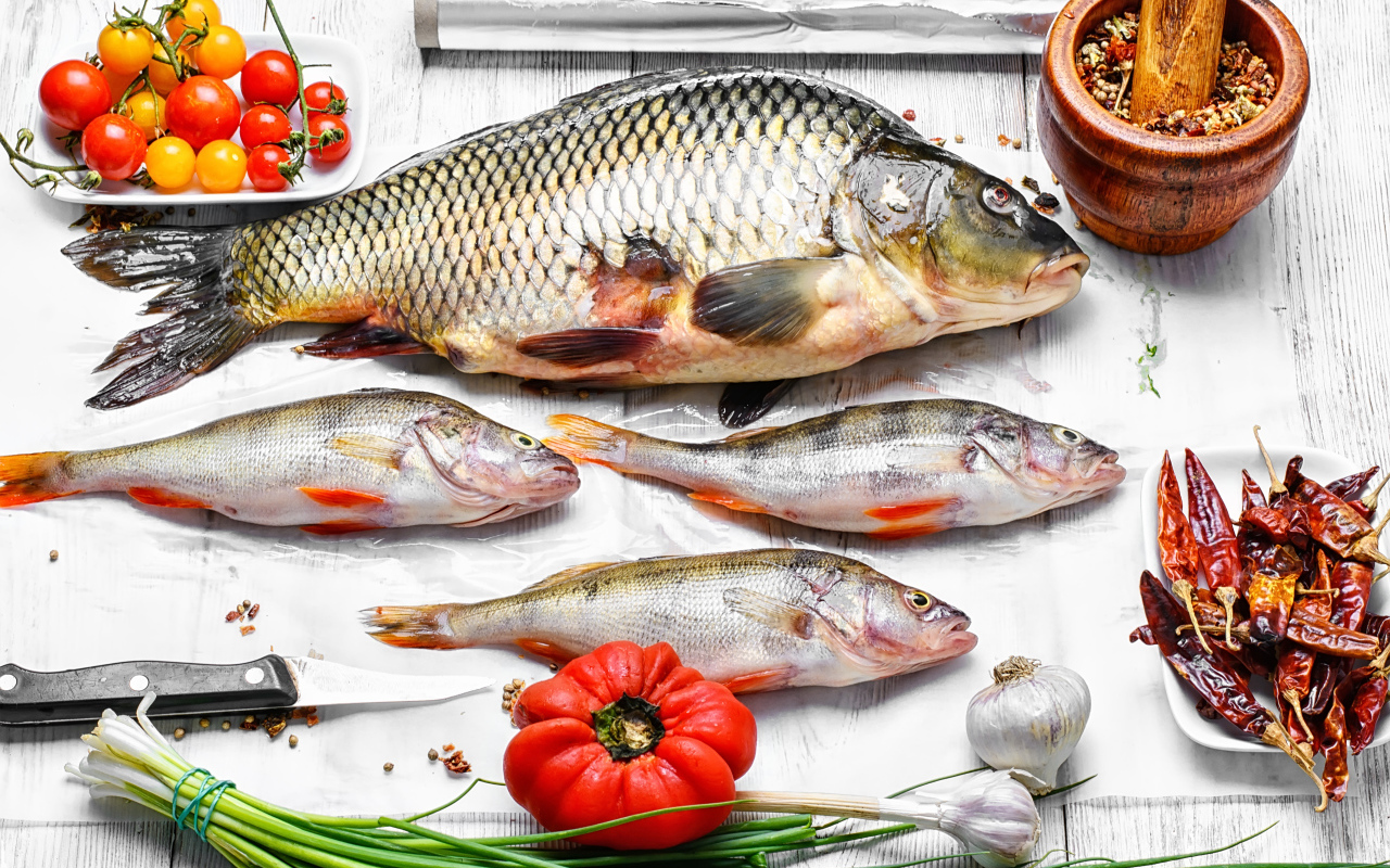 Свежая рыба на столе с помидорами, зеленым луком и  специями