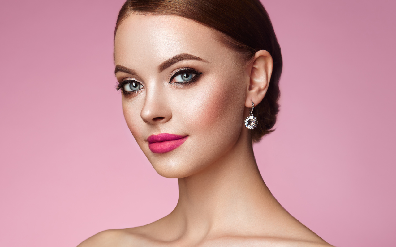 Красивая голубоглазая девушка с красивыми серьгами на розовом фоне