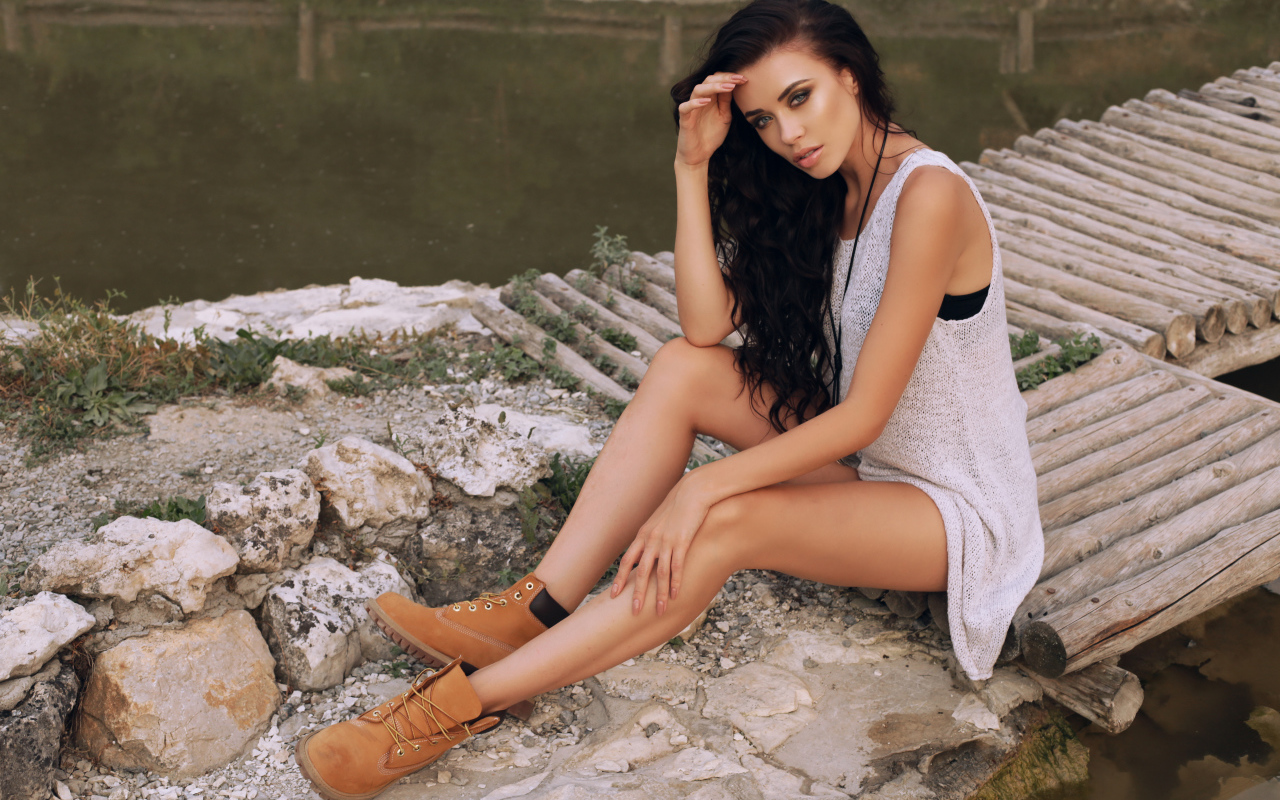 Красивая девушка брюнетка сидит у воды на мостике