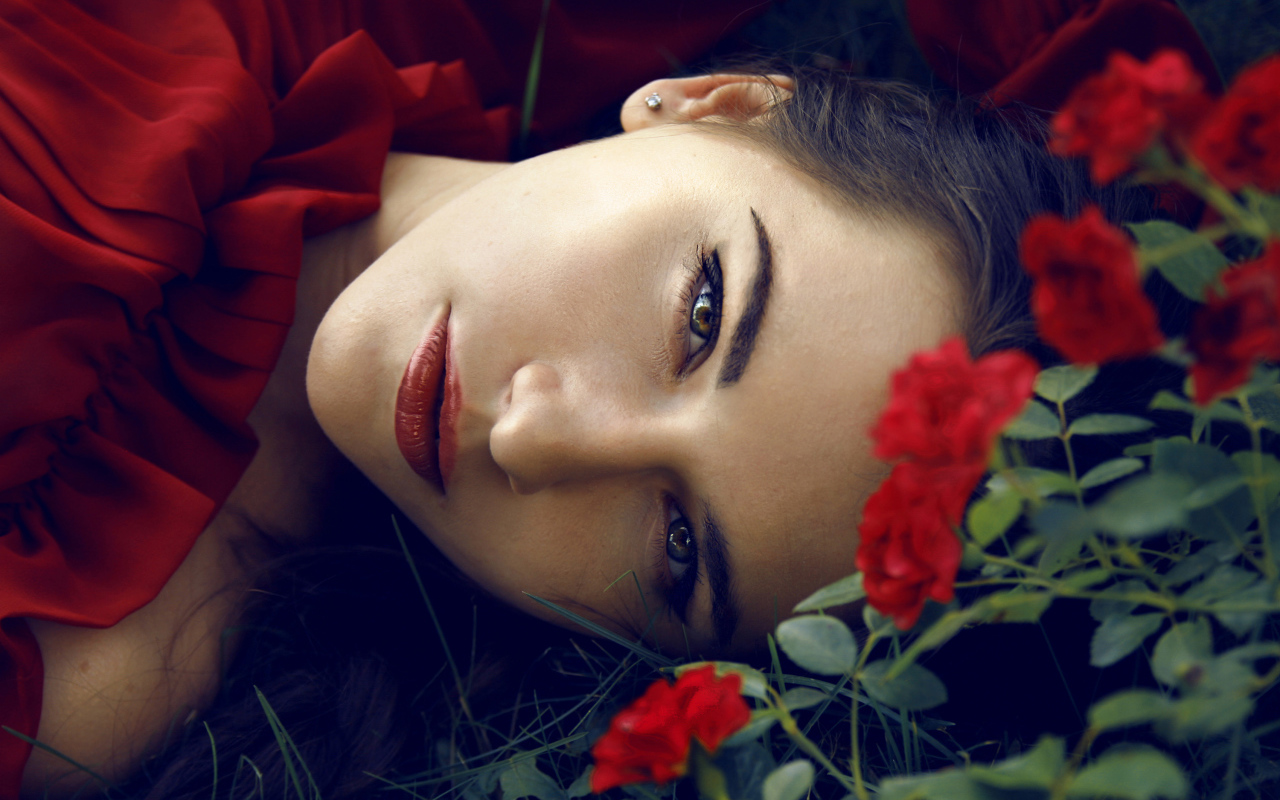 Красивая брюнетка лежит на траве с красными розами