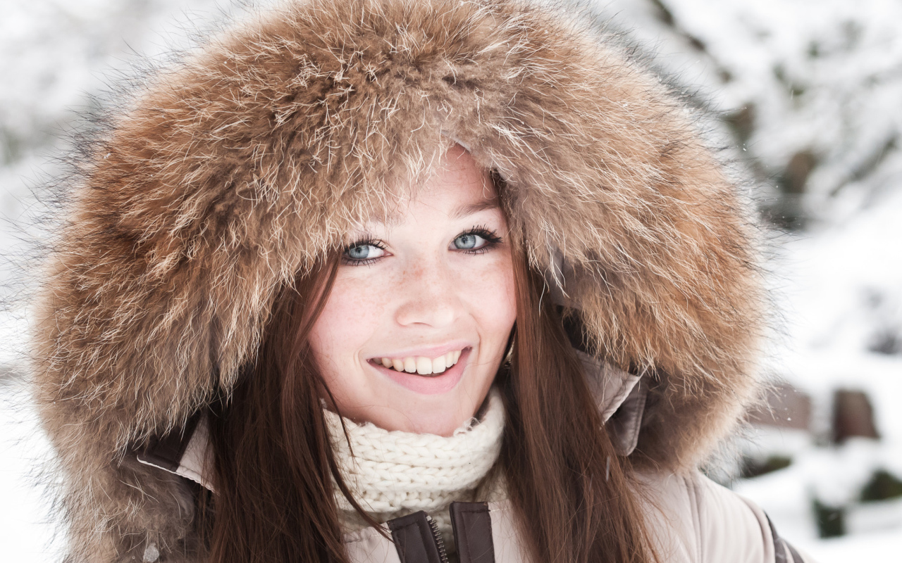 Улыбающаяся голубоглазая девушка в капюшоне зимой