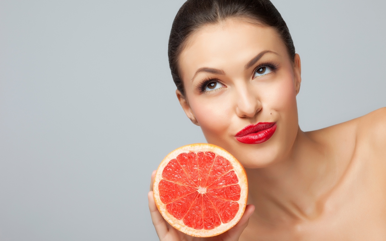 Молодая девушка с красными губами с половиной грейпфрута