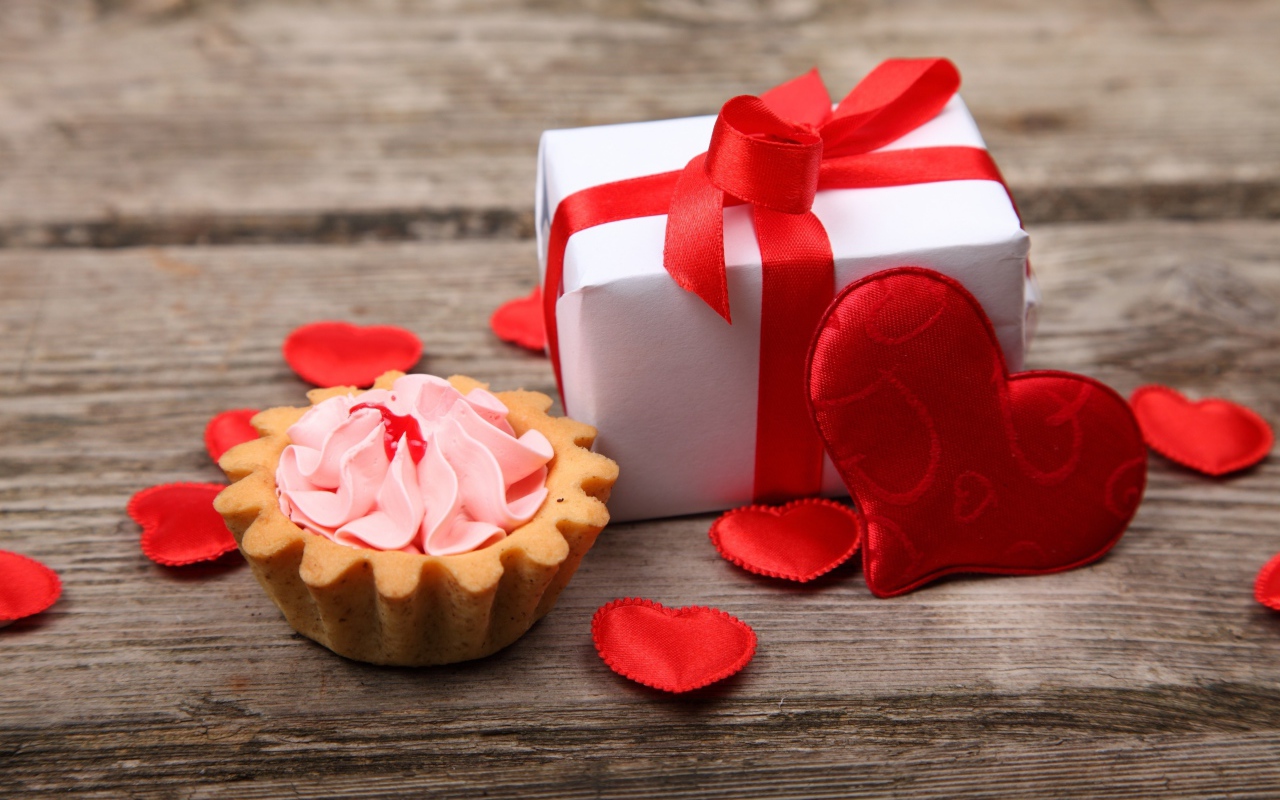 Пирожное, подарок и сердечки на деревянном фоне на День Святого Валентина