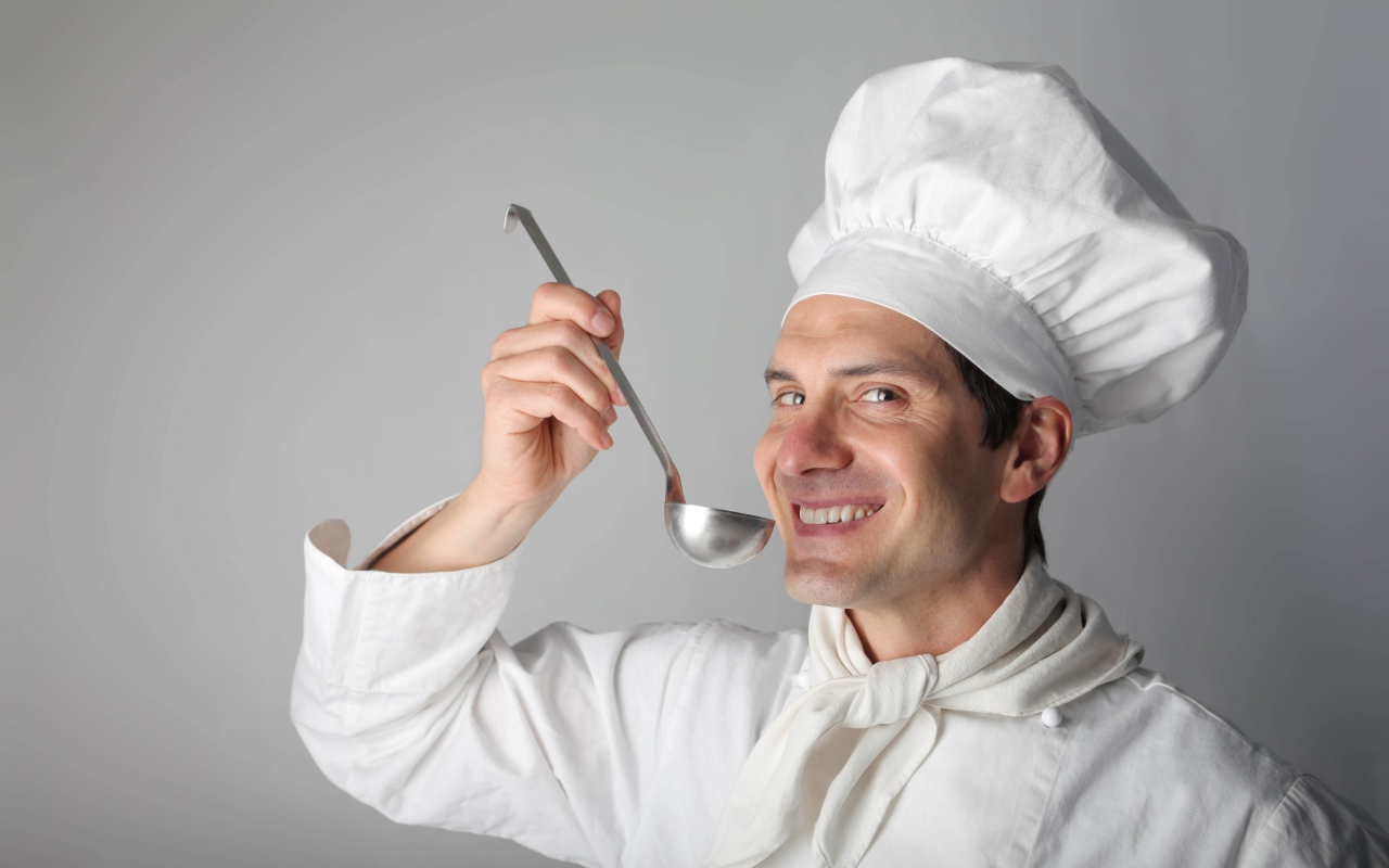 Улыбающийся мужчина повар с половником в руках на сером фоне