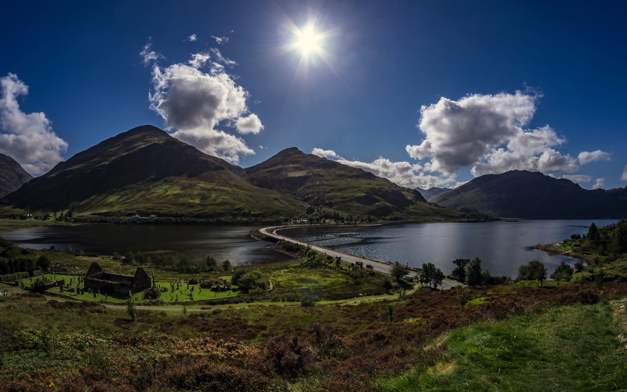 Яркое солнце в голубом небе над горами у реки