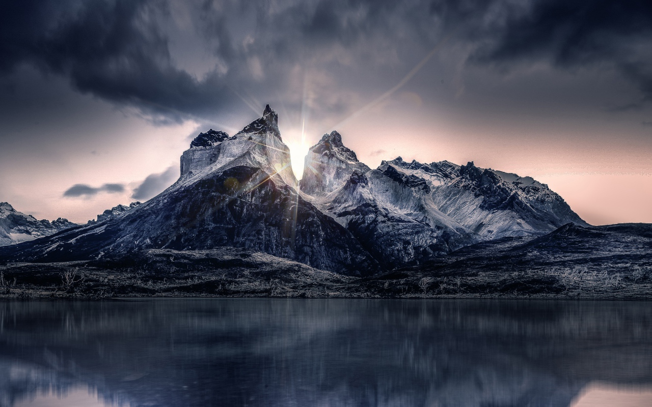 Рассвет солнца над горами у озера под пасмурным небом