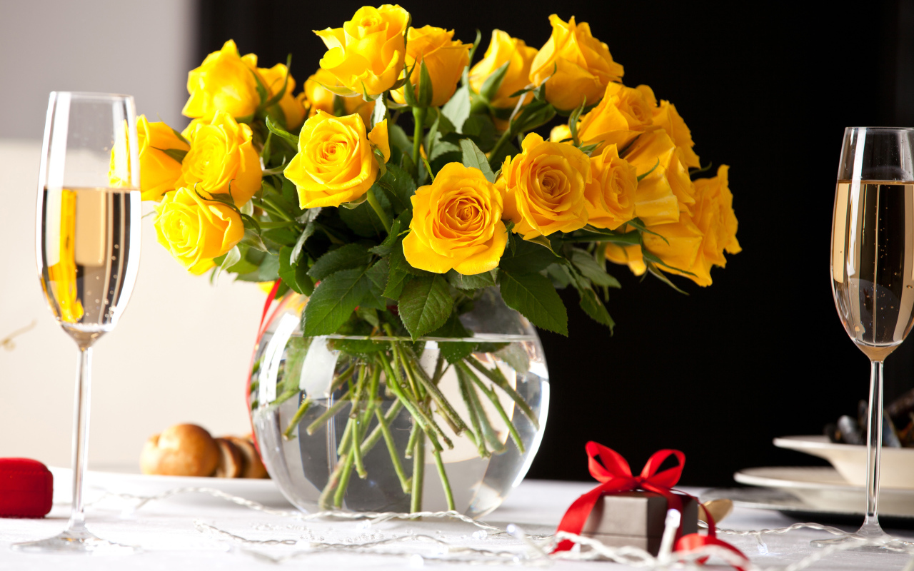 Букет желтых роз в стеклянной вазе с бокалами шампанского на столе