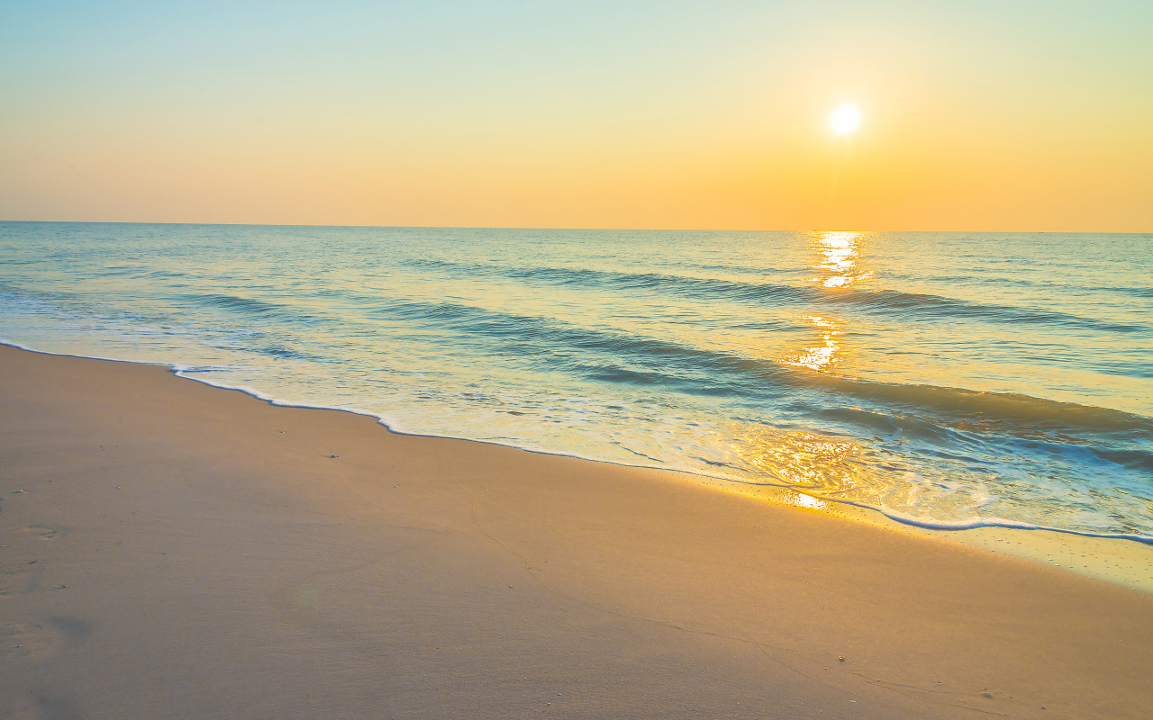 Морские волны на желтом песке на закате солнца летом