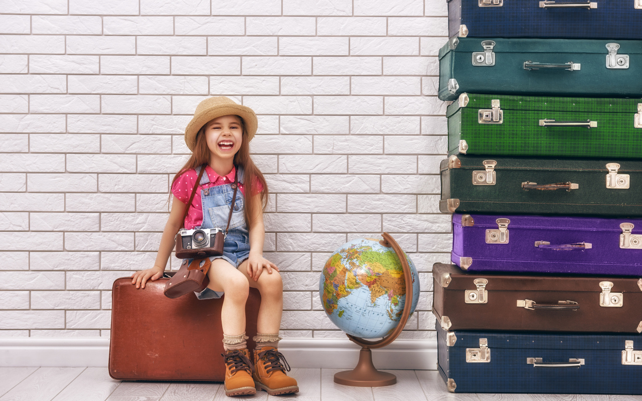 Маленькая девочка с фотоаппаратом сидит на чемодане