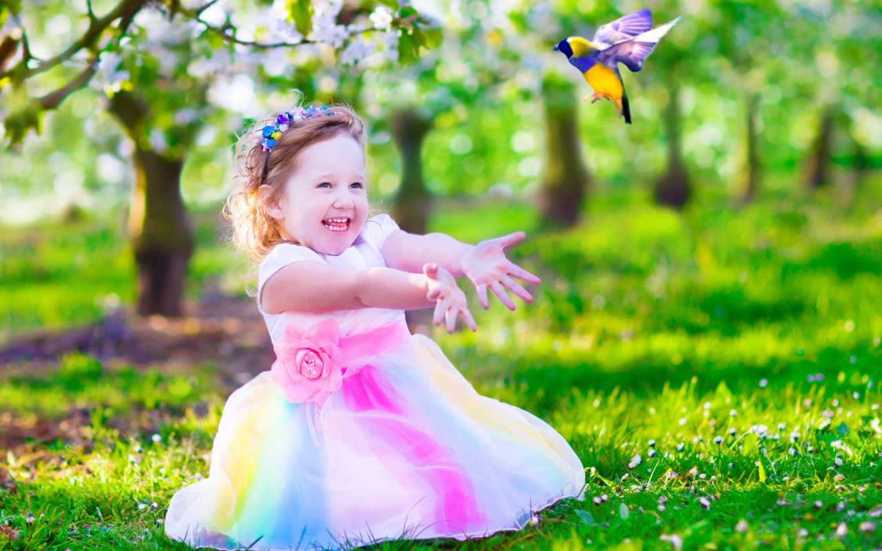 Смеющаяся маленькая девочка в красивом платье на зеленой траве