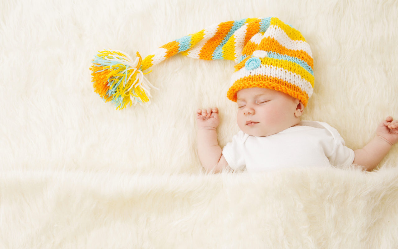 Маленький спящий под меховым покрывалом малыш в вязаной шапке