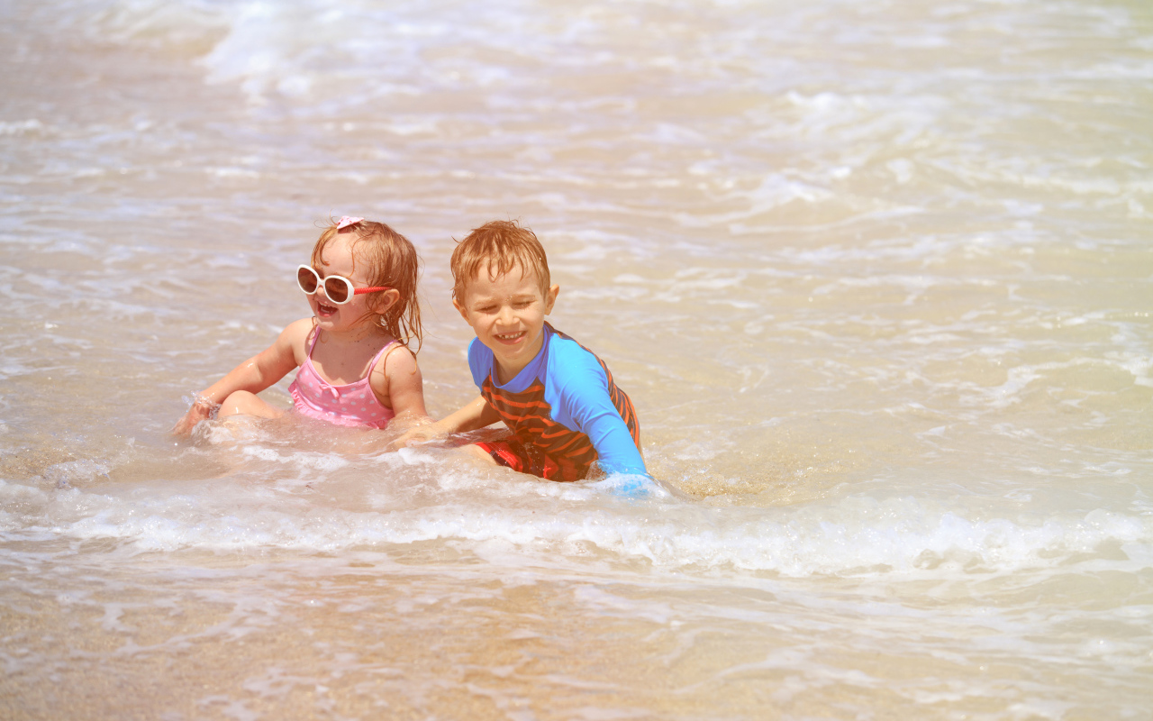 Маленькие мальчик и девочка купаются в море 