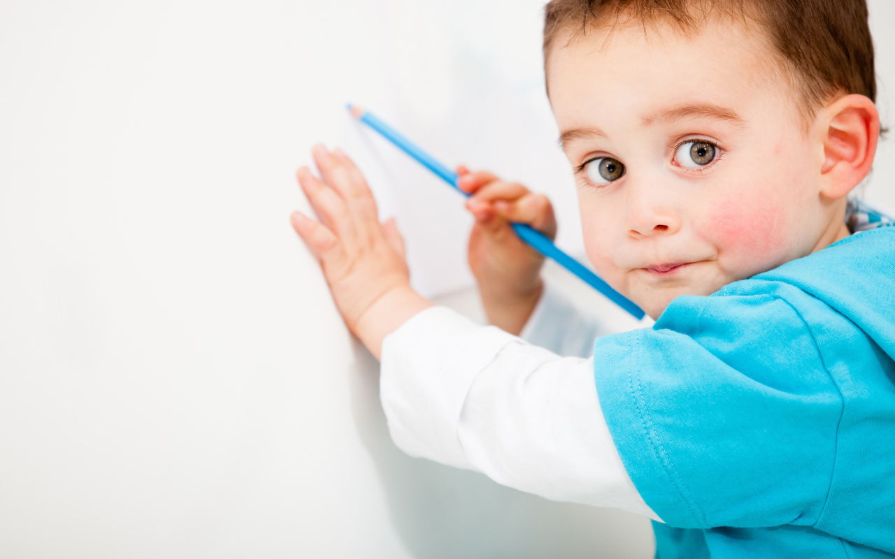 Маленький мальчик рисует карандашом на стене